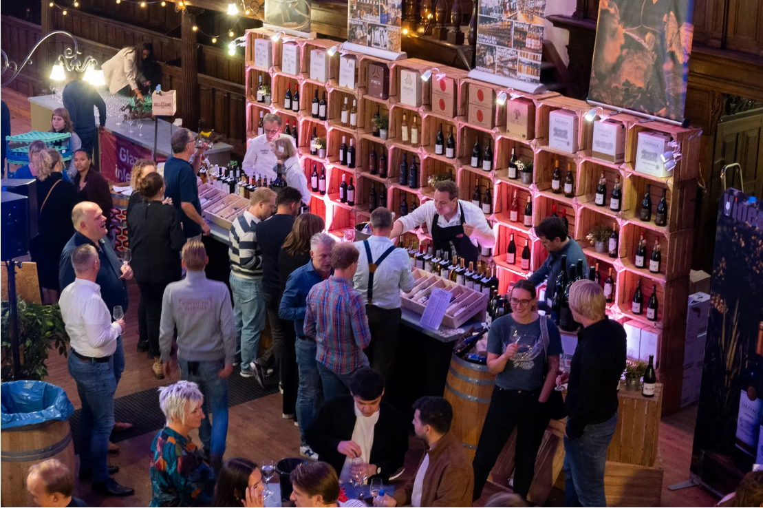 de foto toont een groep mensen die voor een wijnstand staan om daar te kunnen proeven